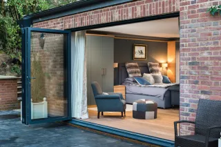 fully open bifold door from the outside looking in to a room with sofas, foot stools and wood flooring