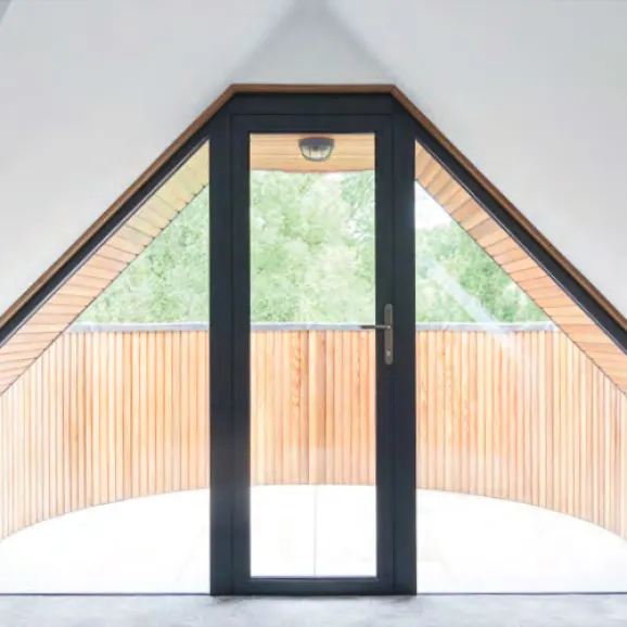 interior view of a black framed bespoke aluminium single door inset into a A shaped curtain wall of windows on either side of the door looking out onto a t