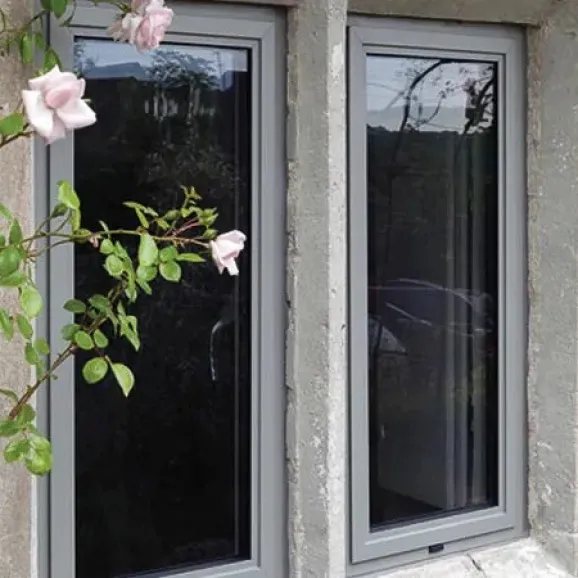 external view of two side by side light grey aluminium framed windows in a stone building framed by pink rose bush to the left of windows