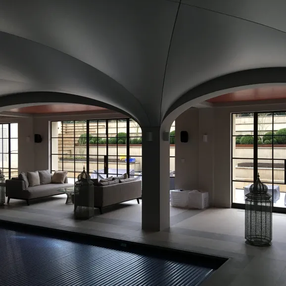 internal view of a covered swimming pool in a pool room. interesting arch vaulted ceiling with a pillar. beyond the pillar there is a sitting area with two