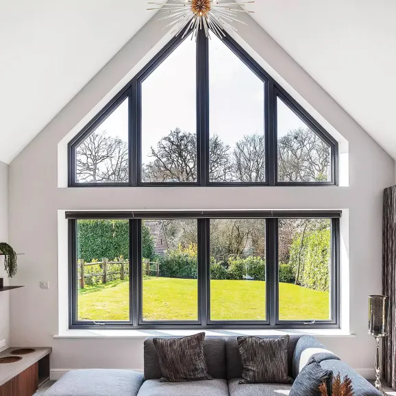 internal view from a living room with a light blue L-shaped sofa with throw pillows looking through a large curtain wall or glazed gable of windows onto a 